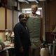 A man in a blue jacket and a very tall man-robot wearing a bow tie stand in a cluttered kitchen in a scene from Brian and Charles.